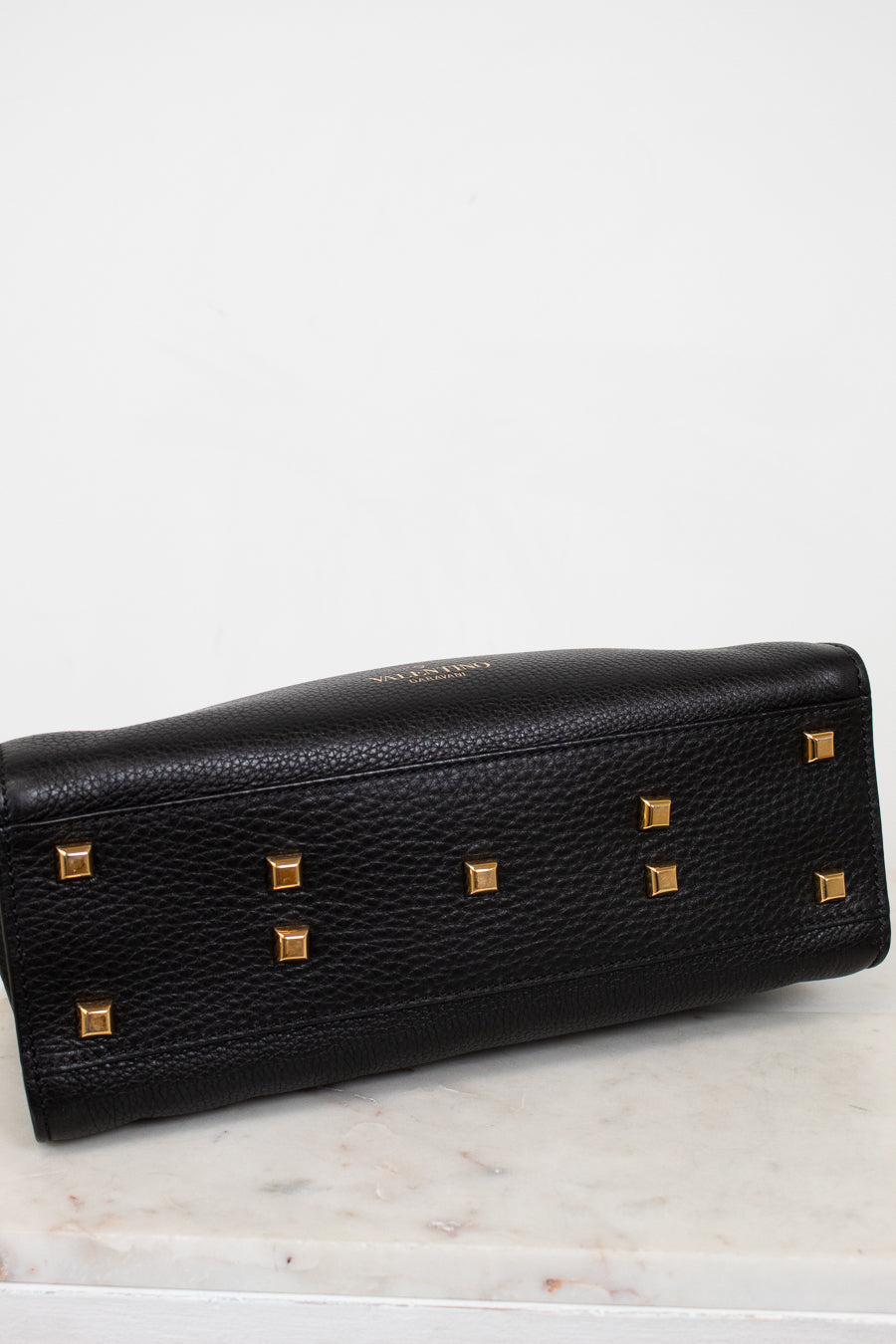 Black leather bottom of purse with gold studs on a marble surface