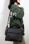 Person wearing a green sweatshirt with white text, holding a black handbag against a plain background