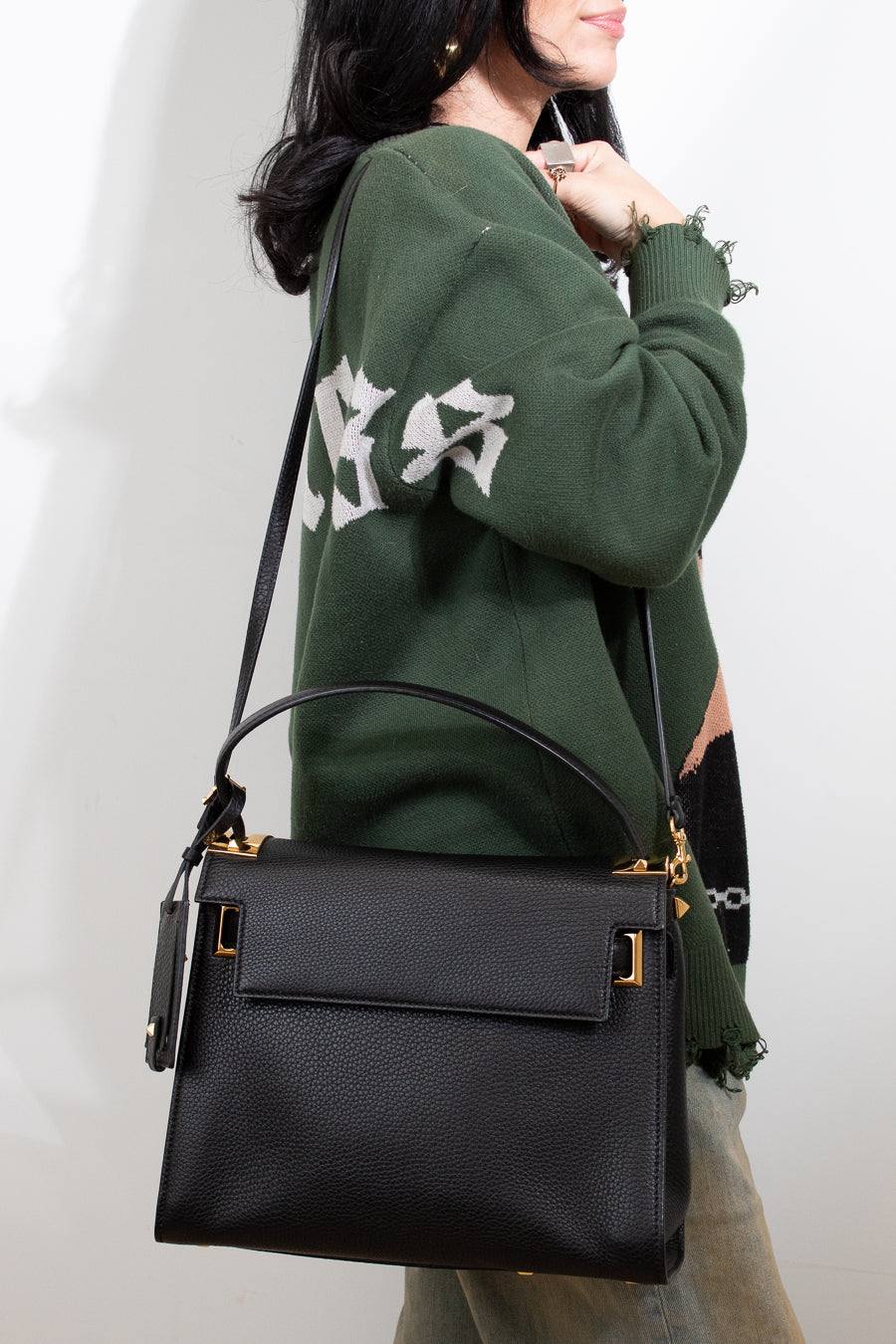 Person wearing a green sweatshirt with white text, holding a black handbag against a plain background