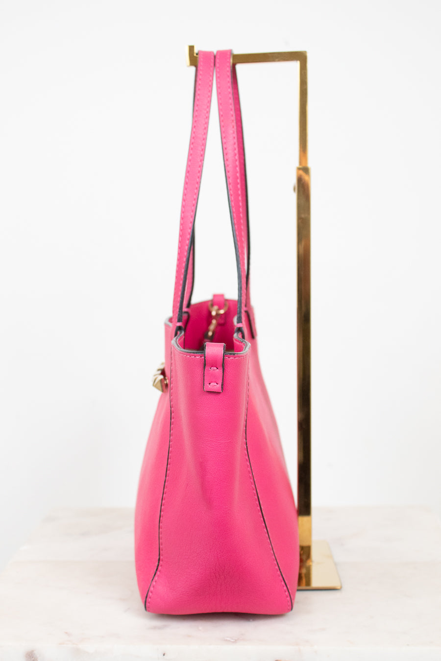 Pink handbag on a gold stand against a white background