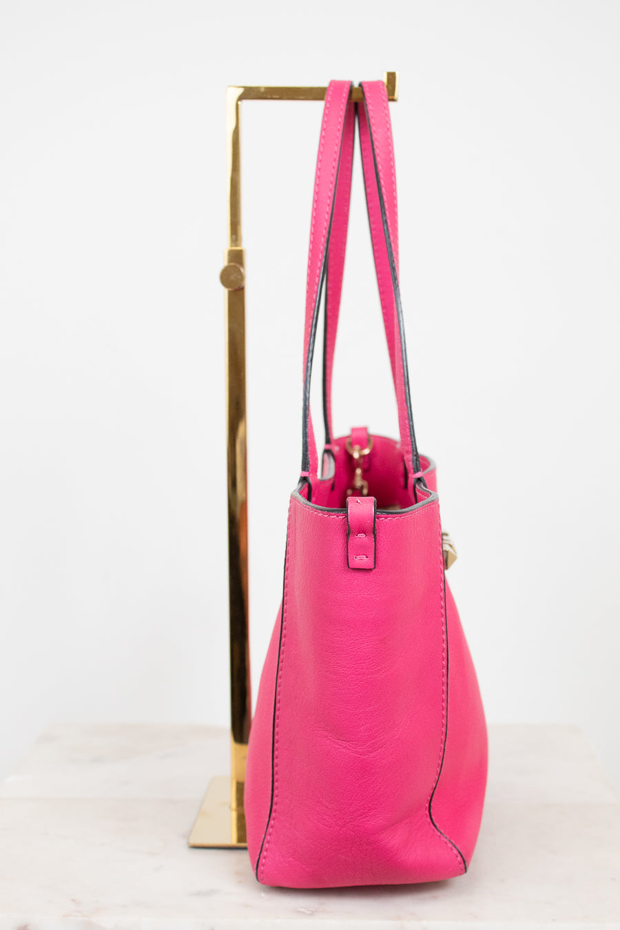 Pink handbag on a gold stand against a white background
