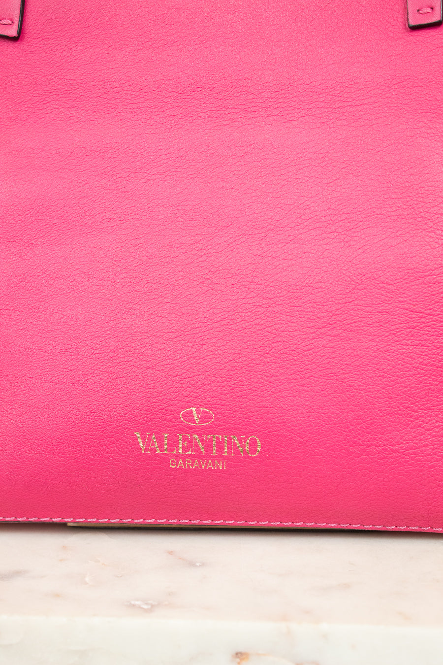 Pink leather handbag with Valentino logo on a light marble surface