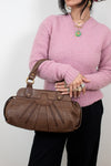 Person wearing a pink sweater holding a brown handbag against a white background