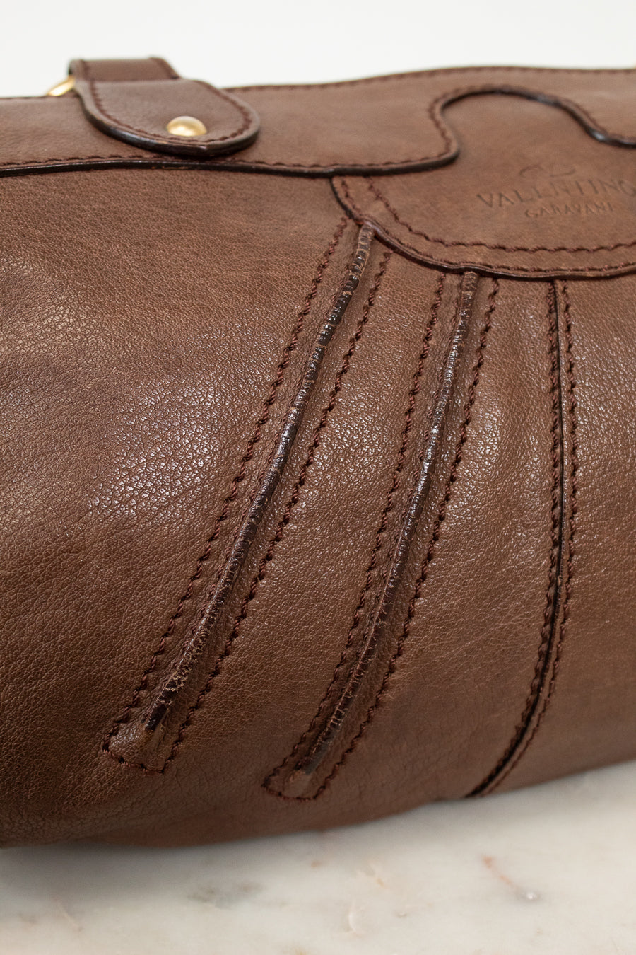 Close-up of a brown leather bag with visible stitching on a marble surface