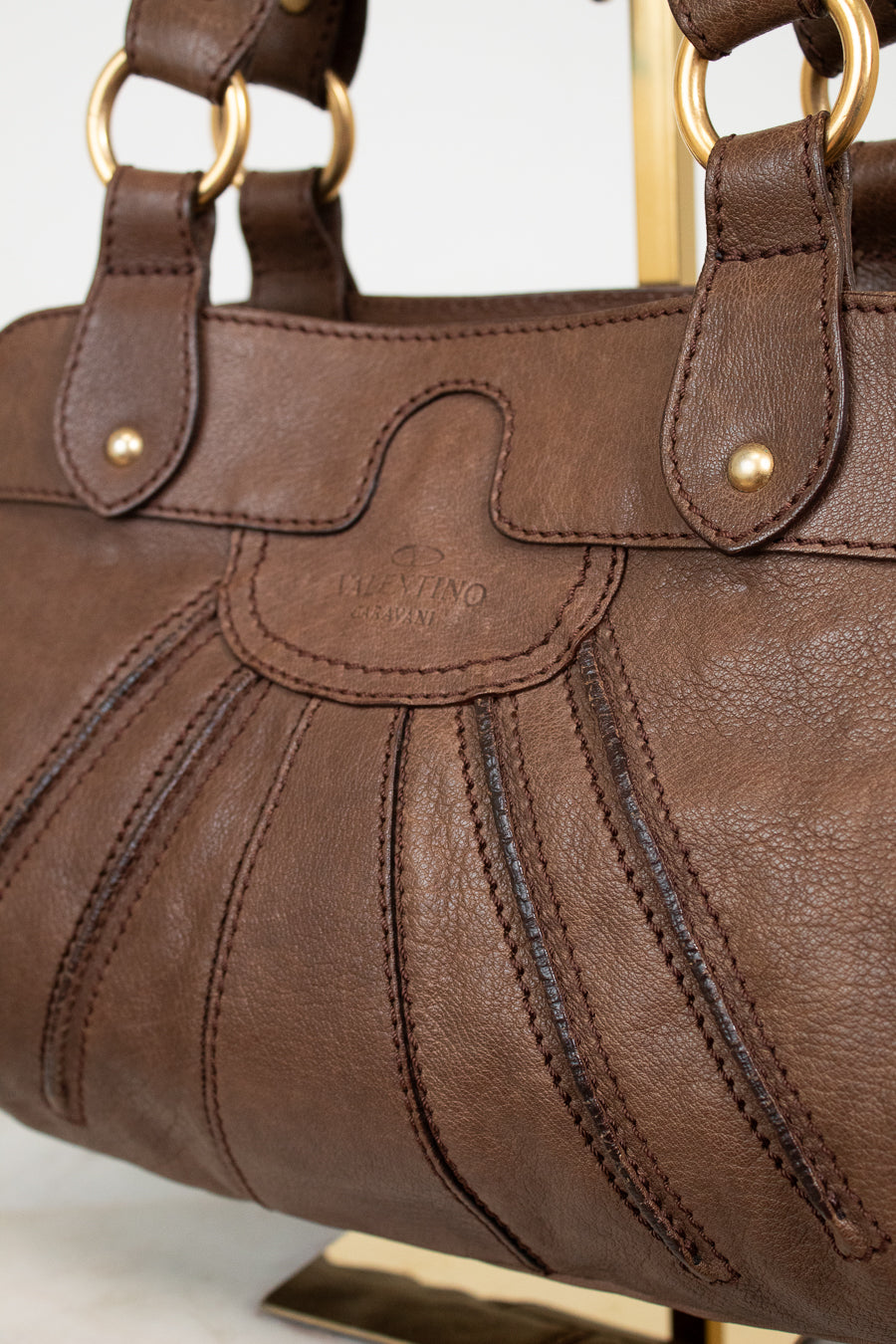 Brown leather handbag with gold accents on a white background
