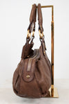 Brown leather handbag with handles on a gold stand against a white background