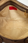 Close-up of a brown leather bag with a gold zipper and red logo tag