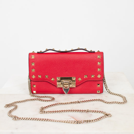 Red rectangular leather bag against a plain  background. Bag is decorated with gold-tone rock-stud details and a chain as well as a studded top handle.