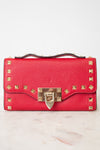 Close-up of red rectangular leather bag decorated with gold-tone rock-stud details and top handle against a plain background