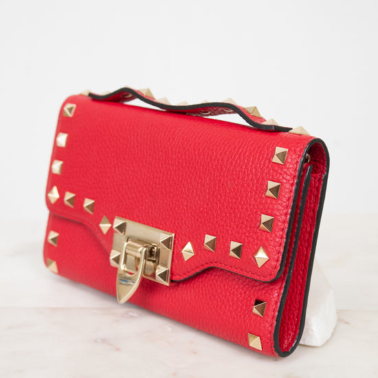 Side view of red rectangular leather bag decorated with gold-tone rock-stud details and top handle against a plain background