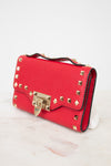 Side view of red rectangular leather bag decorated with gold-tone rock-stud details and top handle against a plain background