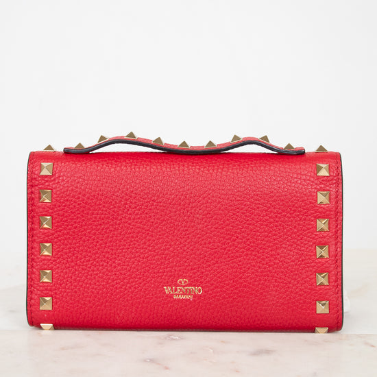 Back close-up view of red rectangular leather bag decorated with gold-tone rock-stud details and top handle against a plain background