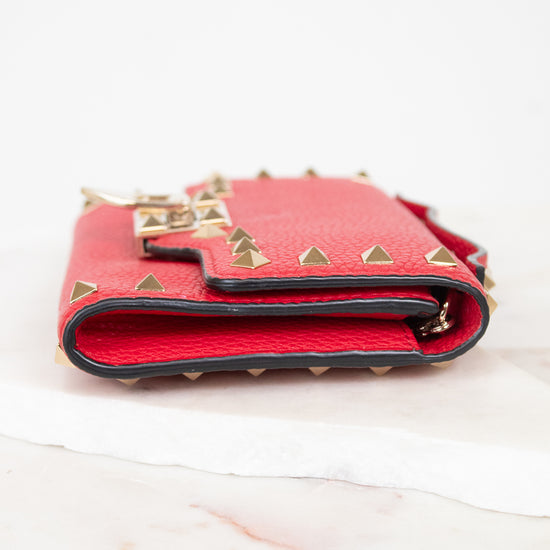 Side view of red rectangular leather bag decorated with gold-tone rock-stud details laying on marble surface.