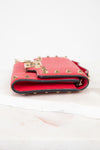 Side view of red rectangular leather bag decorated with gold-tone rock-stud details laying on marble surface.