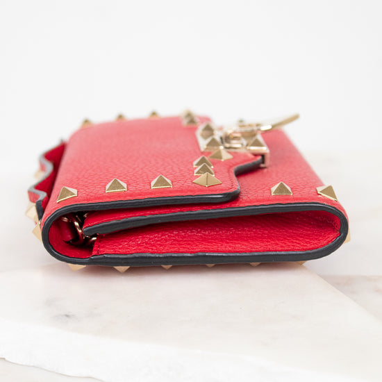 Side view of red rectangular leather bag decorated with gold-tone rock-stud details laying on marble surface.
