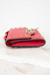 Side view of red rectangular leather bag decorated with gold-tone rock-stud details laying on marble surface.