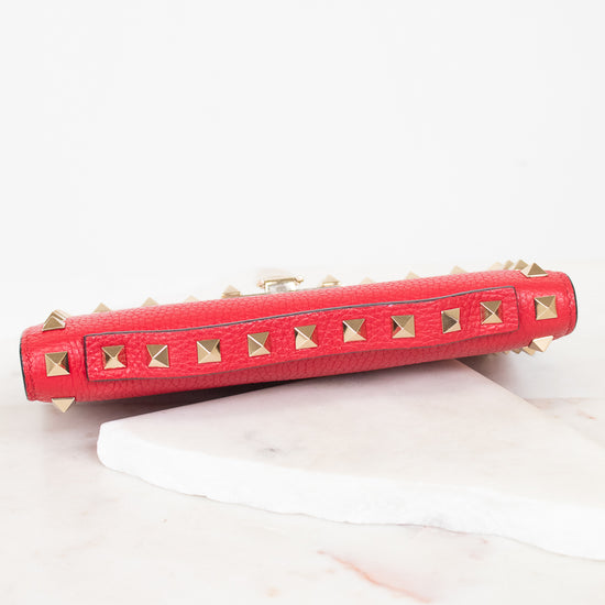 Top view of red rectangular leather bag decorated with gold-tone rock-stud details showing top handle detail and laying on marble surface.