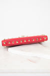 Top view of red rectangular leather bag decorated with gold-tone rock-stud details showing top handle detail and laying on marble surface.