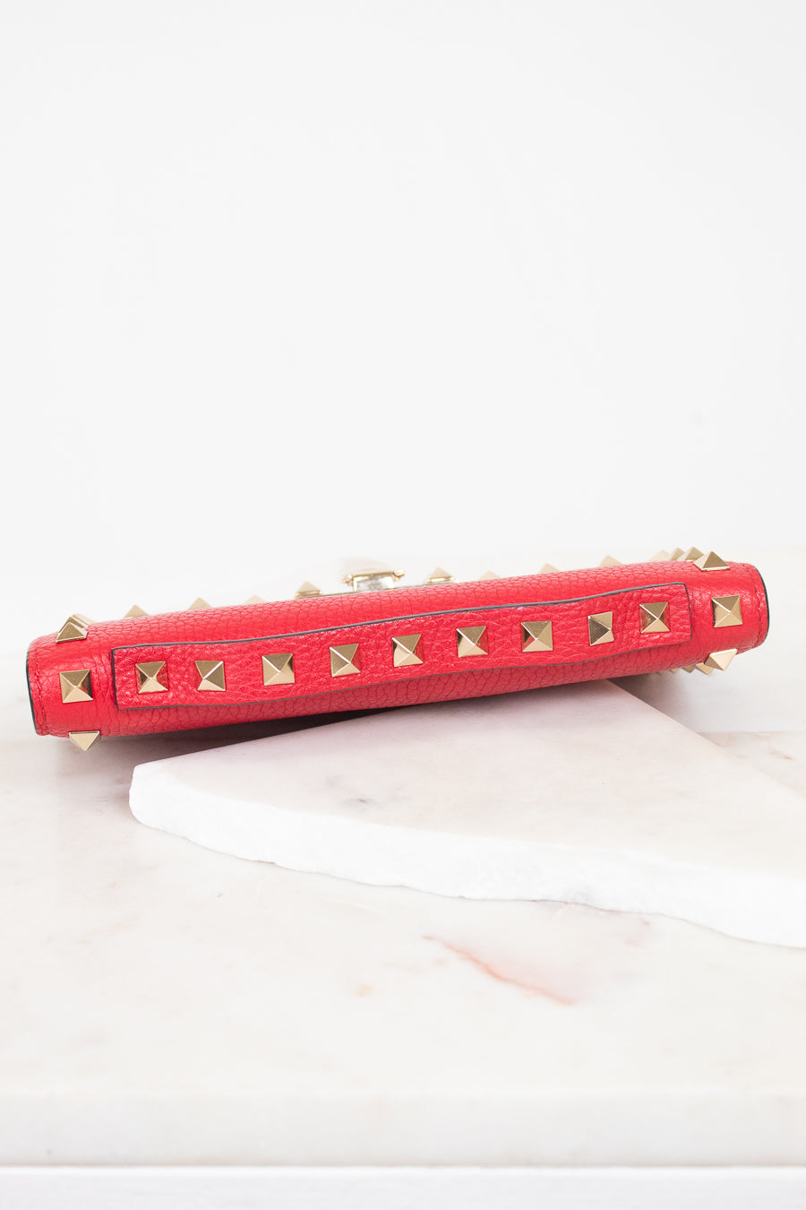 Top view of red rectangular leather bag decorated with gold-tone rock-stud details showing top handle detail and laying on marble surface.