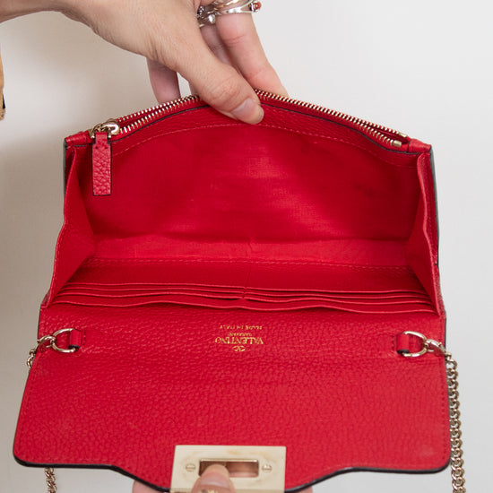 Hands holding red leather chain bag opened showing card organization slots and interior zipper compartment