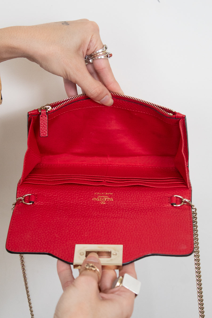 Hands holding red leather chain bag opened showing card organization slots and interior zipper compartment