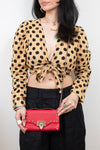 Woman wearing black pants and polka dot top using crossbody chain strap to hold a red rectangular rock-stud detail bag