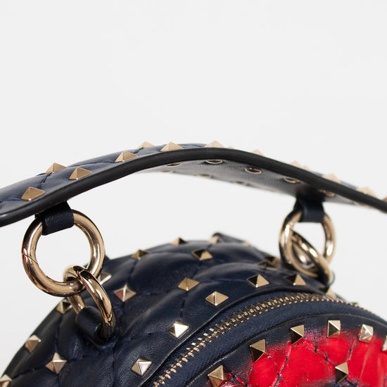 Close-up of a navy blue studded leather handbag with gold-tone hardware and a red pattern visible through the front.