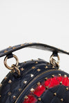 Close-up of a navy blue studded leather handbag with gold-tone hardware and a red pattern visible through the front.