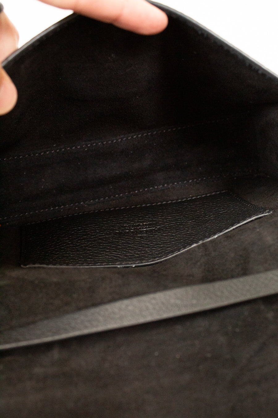 Close-up of a black leather bag with a hand holding it open.