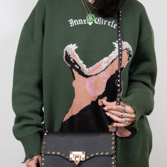 Person wearing a green sweater with a graphic design, holding a black handbag.