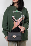 Person wearing a green sweater with a graphic design, holding a black handbag.