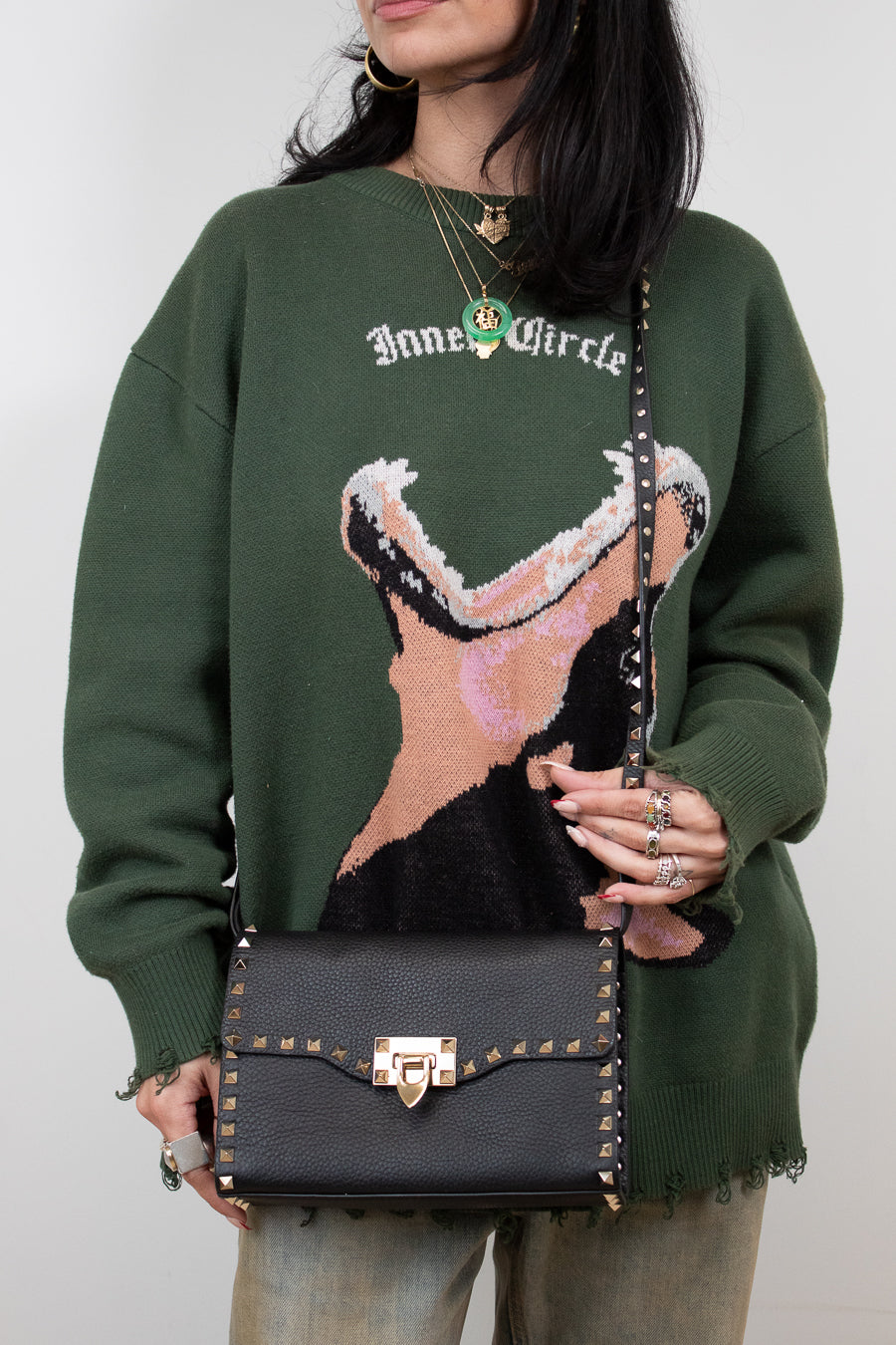 Person wearing a green sweater with a graphic design, holding a black handbag.