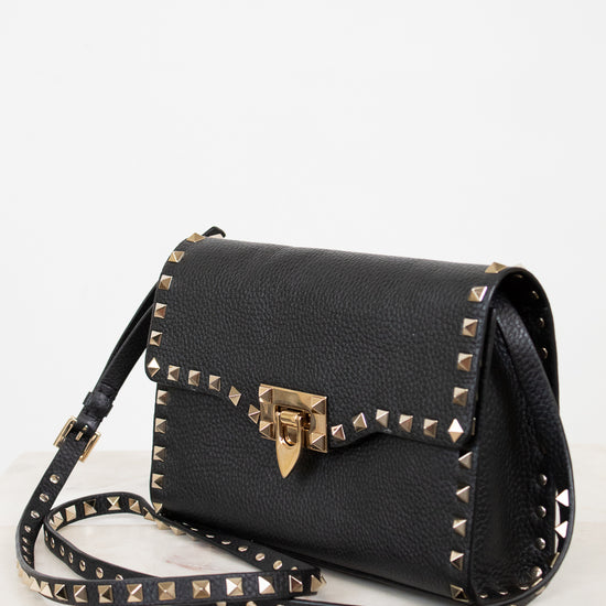 Black handbag with gold studs and a clasp on a white background