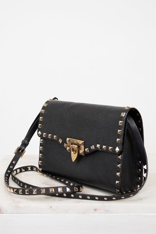 Black handbag with gold studs and a clasp on a white background