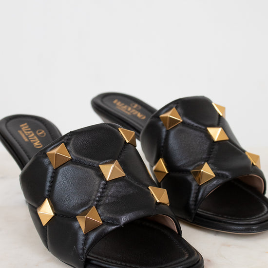 Black sandals with gold studs on a light background