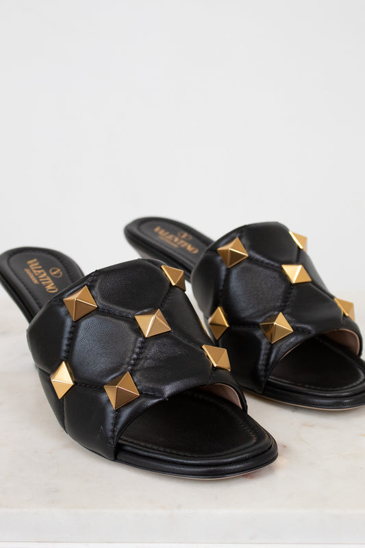 Black sandals with gold studs on a light background