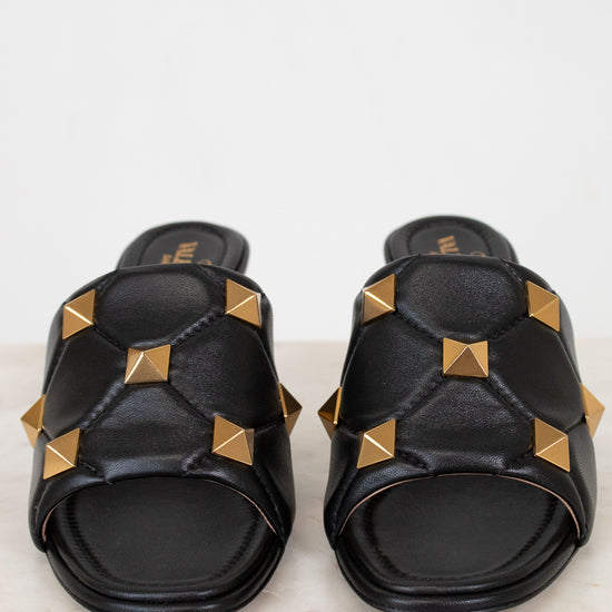 Black slides with gold pyramid studs on a light background