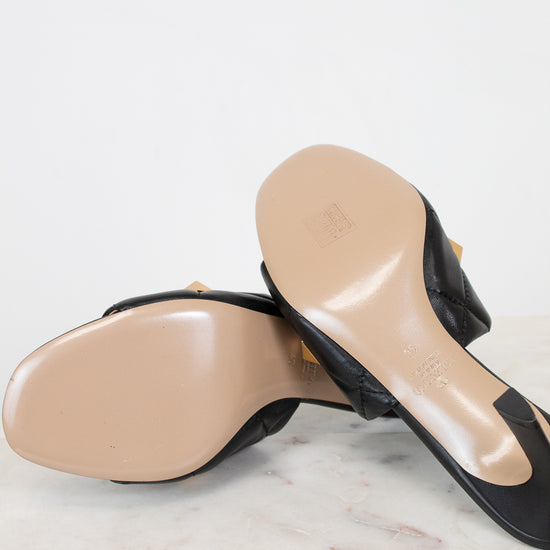 Pair of black high-heeled shoes with beige soles on a light marble surface.