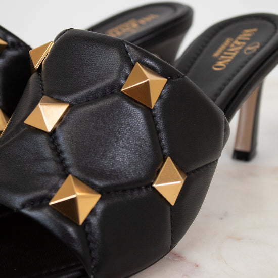 Black high-heeled shoes with gold studs on a light background