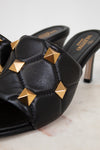 Black high-heeled shoes with gold studs on a light background