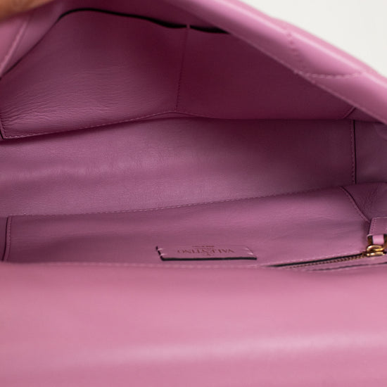 Close-up of the interior of a pink leather handbag, showing a zippered compartment and a small interior label, with a hand holding the open flap at the top left.