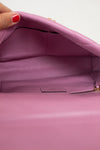 Close-up of the interior of a pink leather handbag, showing a zippered compartment and a small interior label, with a hand holding the open flap at the top left.
