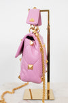 A pink quilted leather handbag with gold pyramid studs and a gold chain strap, displayed on a gold stand against a white background.