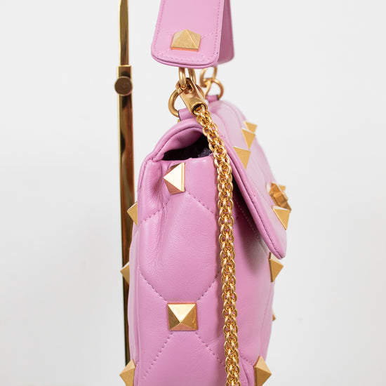 A pink quilted leather handbag with pyramid studs and a gold chain strap, displayed on a gold stand against a white background.