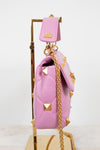 A pink quilted leather handbag with pyramid studs and a gold chain strap, displayed on a gold stand against a white background.