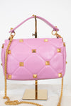 Pink quilted leather handbag with gold pyramid studs and a gold chain strap, displayed on a gold stand against a white background.