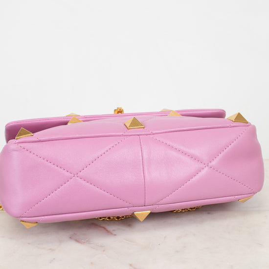 A pink quilted leather handbag with gold pyramid studs, shown from the bottom and laying on a light marble surface against a white background.