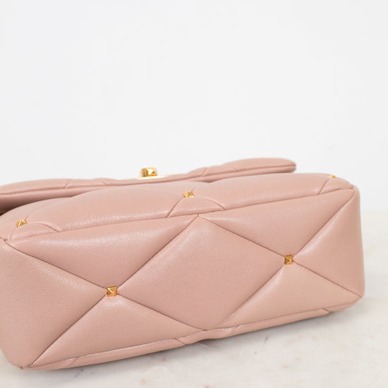 Pink quilted handbag with gold studs on a marble surface