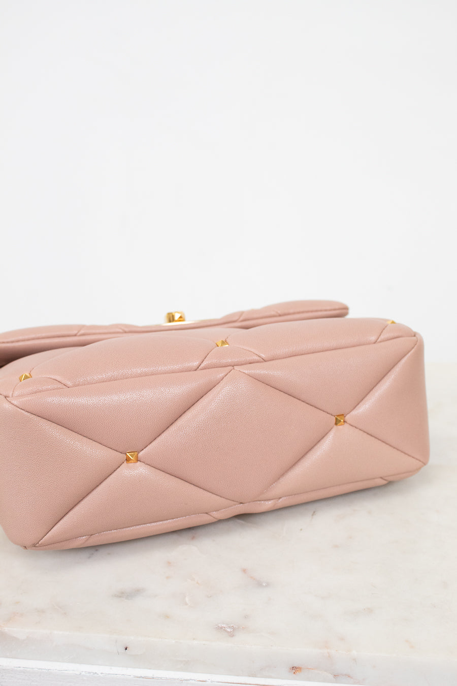 Pink quilted handbag with gold studs on a marble surface