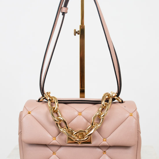 Pink quilted handbag with gold chain detail on a white background